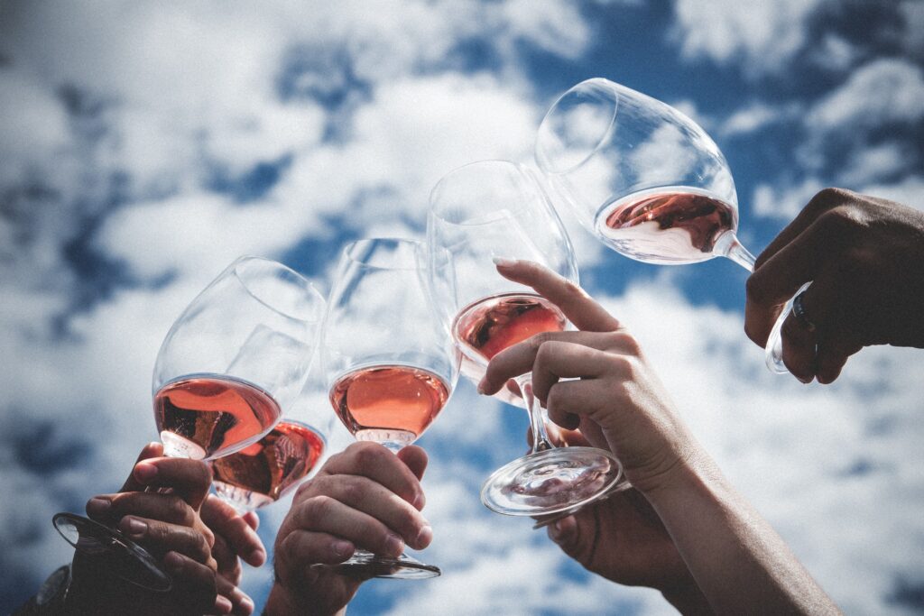 Five hands clinking glasses of rosé wine against a cloudy blue sky, celebrating together—an experience made even more memorable with the Ultimate Evergreen Family Wines Club.