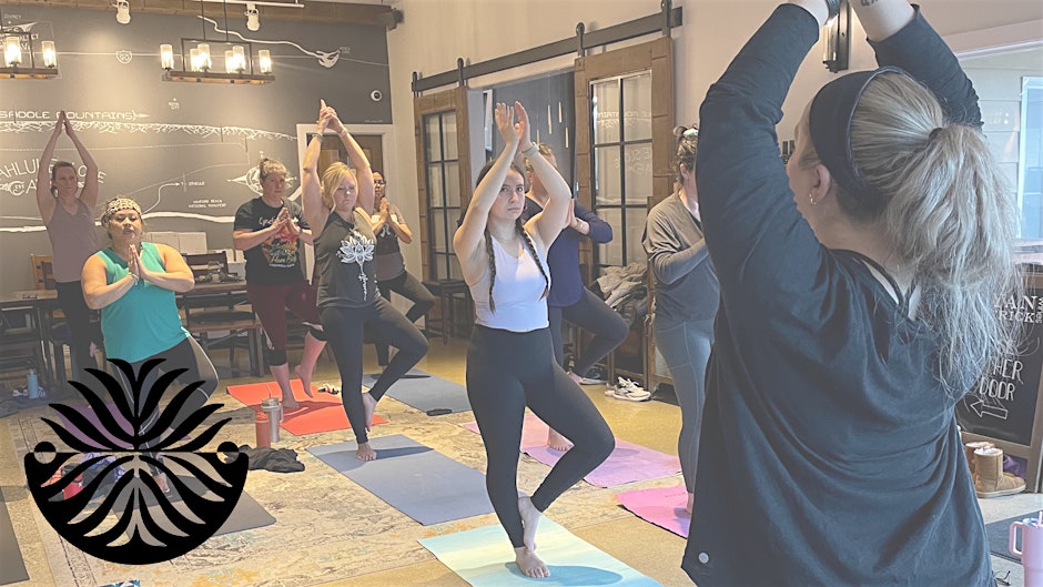 A group of women practice yoga poses together indoors on colorful mats, with a logo in the bottom left corner.