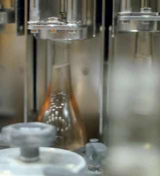 winery-second-vid-poster Close-up of a glass bottle being filled with liquid on an industrial production line.