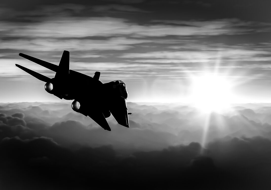 Silhouette of a jet flying above clouds with the sun rising or setting in the background.